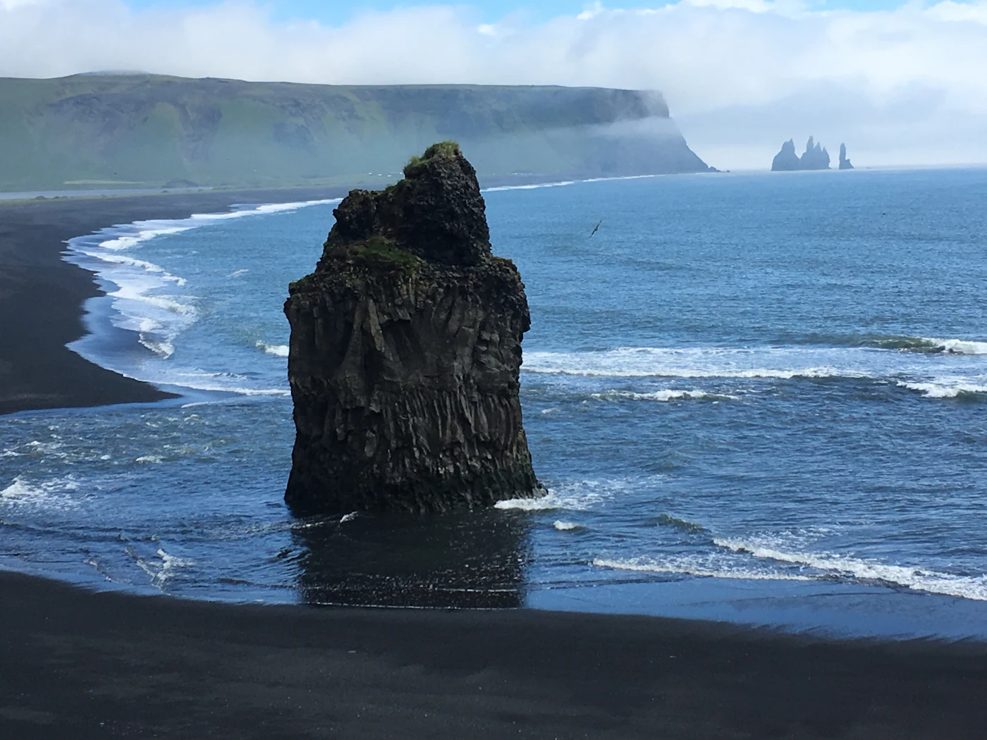 A single black sea stack beside a long curving beach