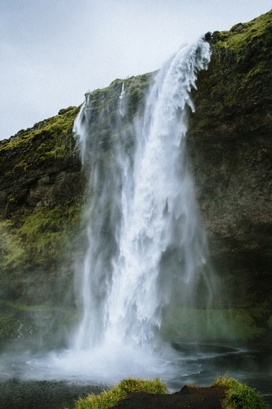 A tall waterfall falling beside a green cliff