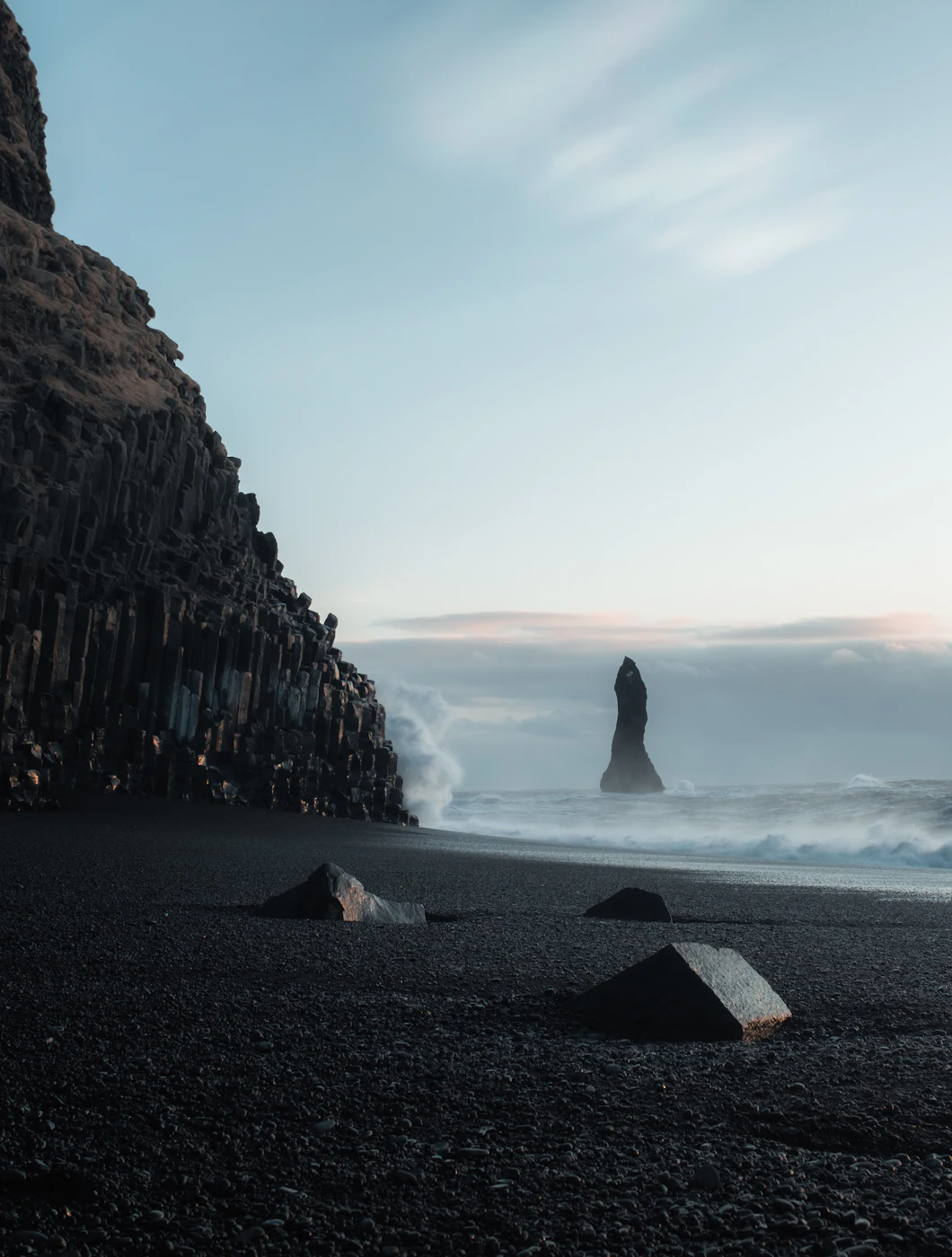 Sea stacks rising offshore beyond a dark cliff