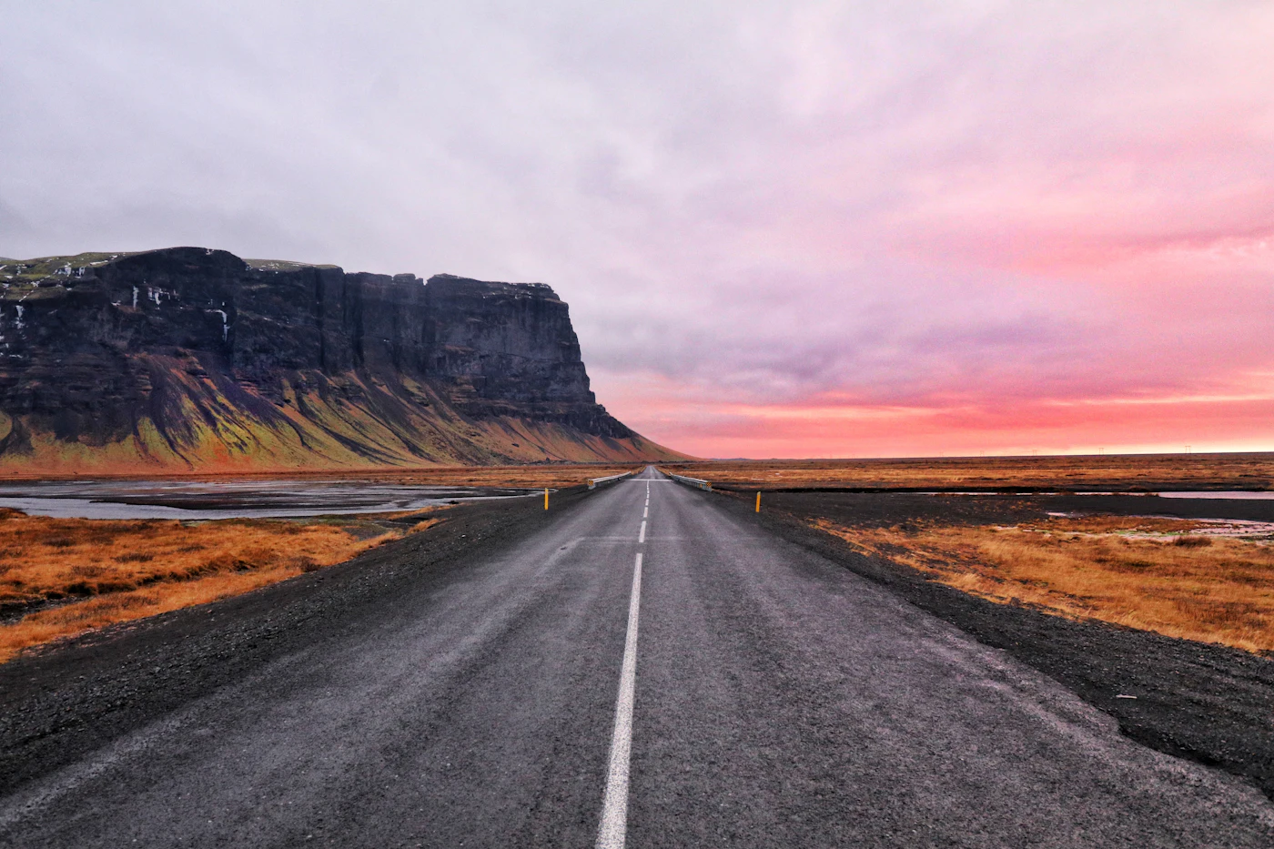 An empty road beneath a cliff at a pink dawn