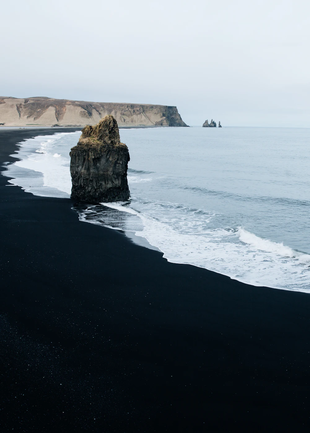 A sea stack standing off a black sand beach near Vík
