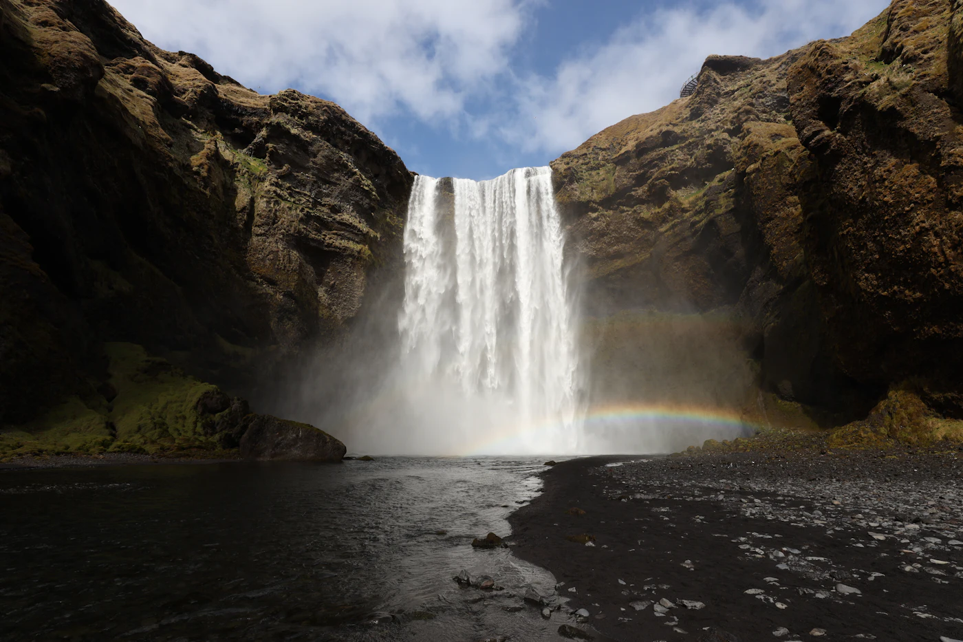 Skógafoss under a blue sky with mist rising from the pool