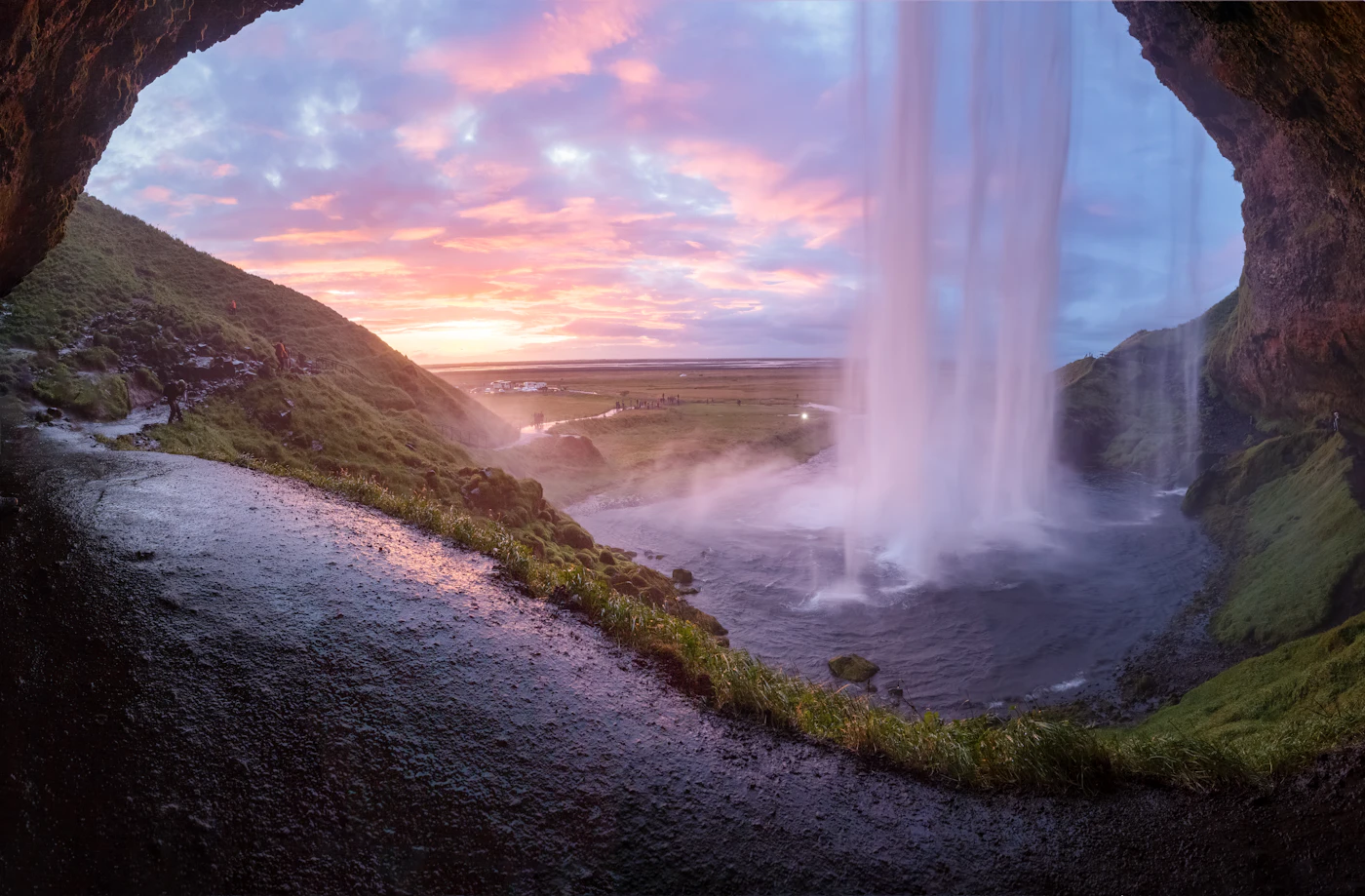 A pink midnight sky framed by the cave behind Seljalandsfoss