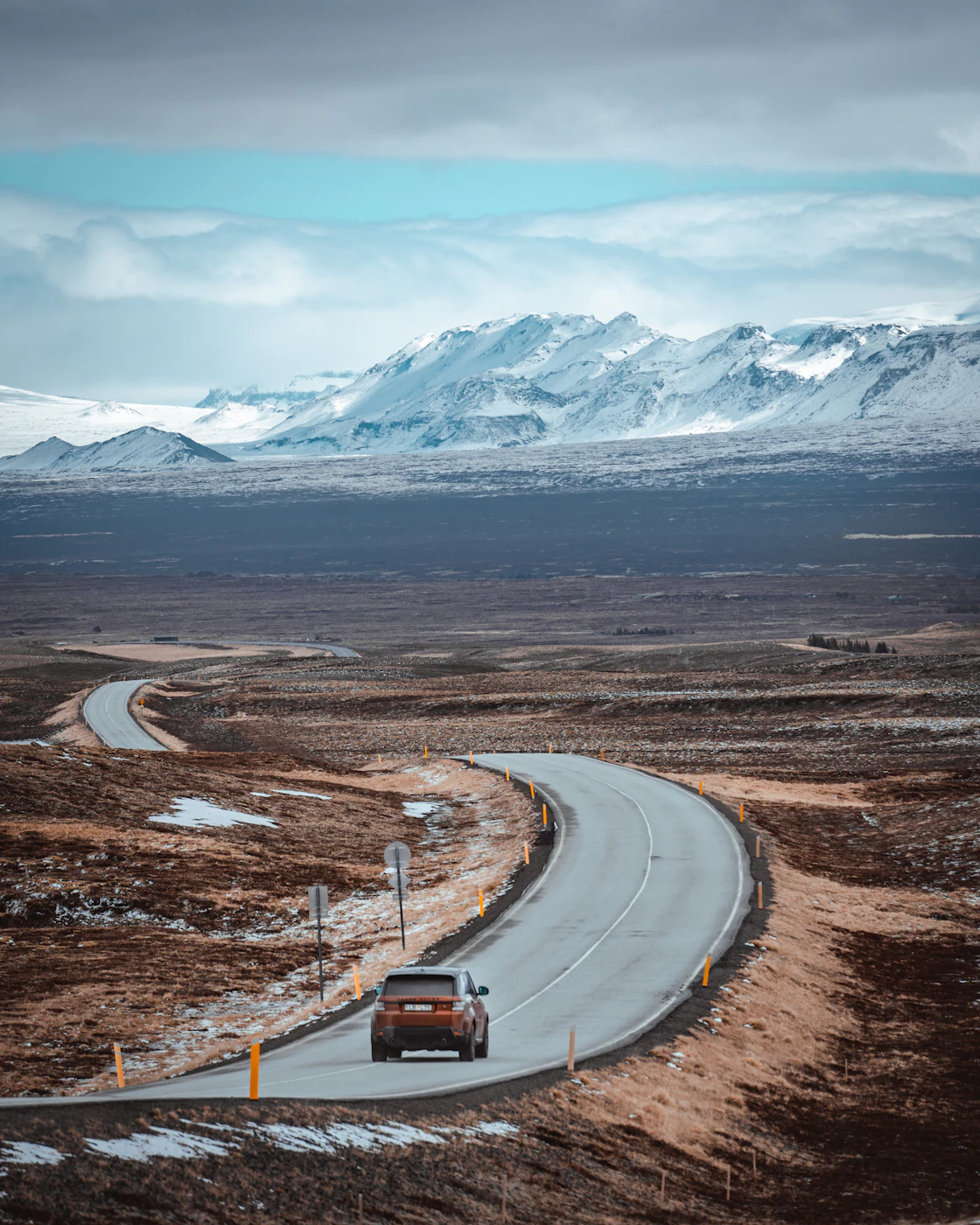 A car on a winding road below snowy mountains