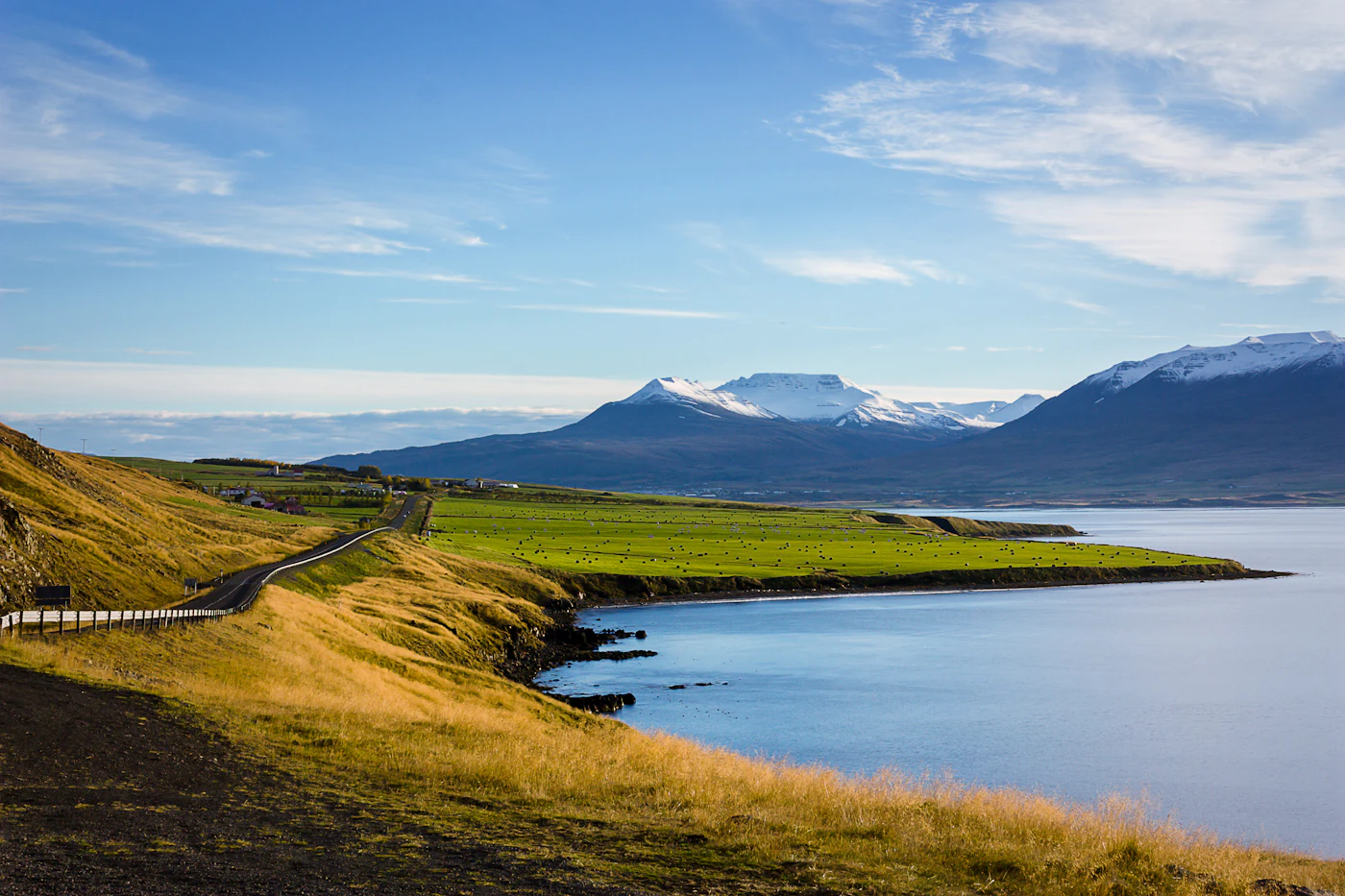 A calm lake with green fields and distant mountains