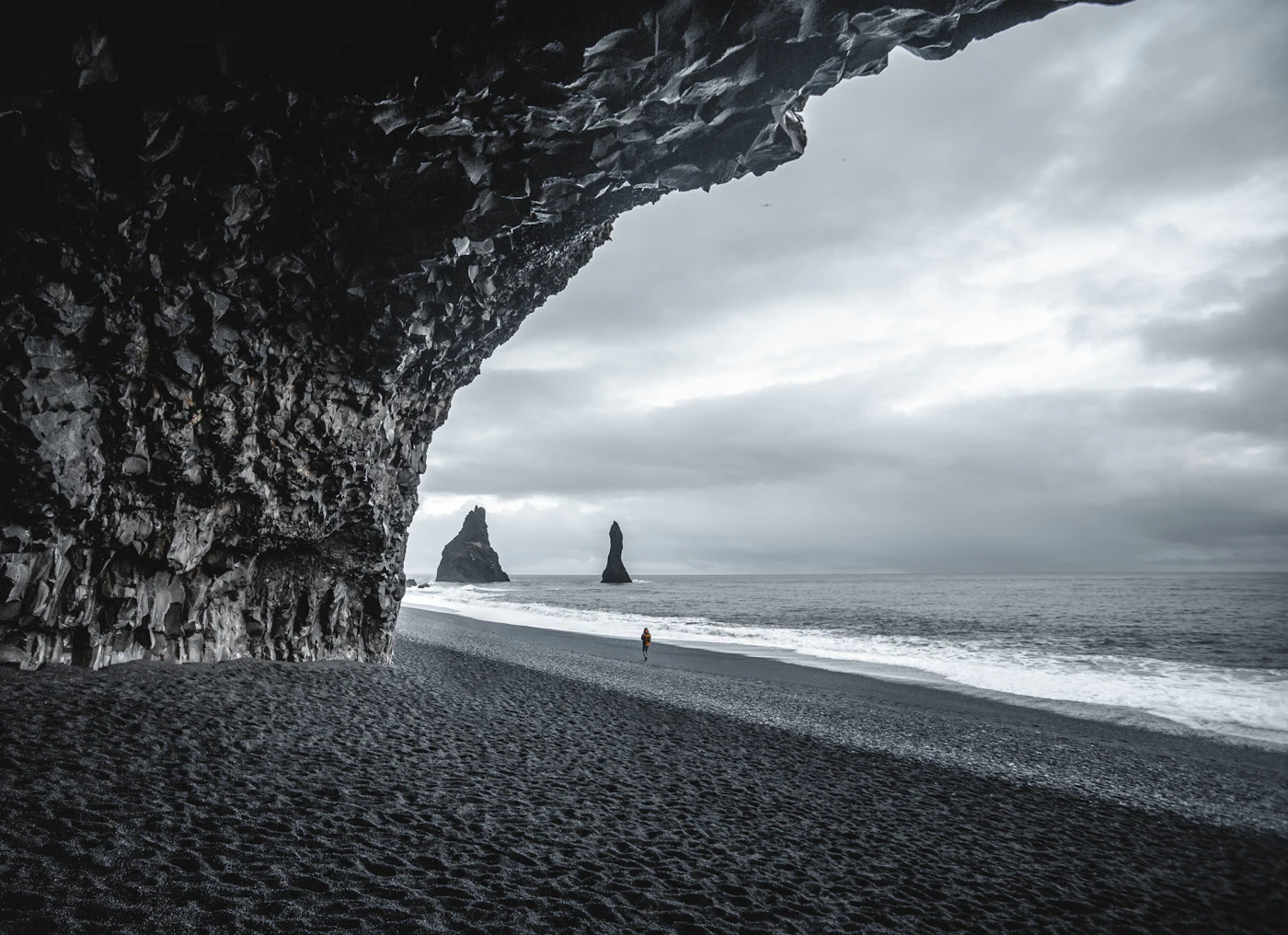A person walking along the shore beneath a cave arch